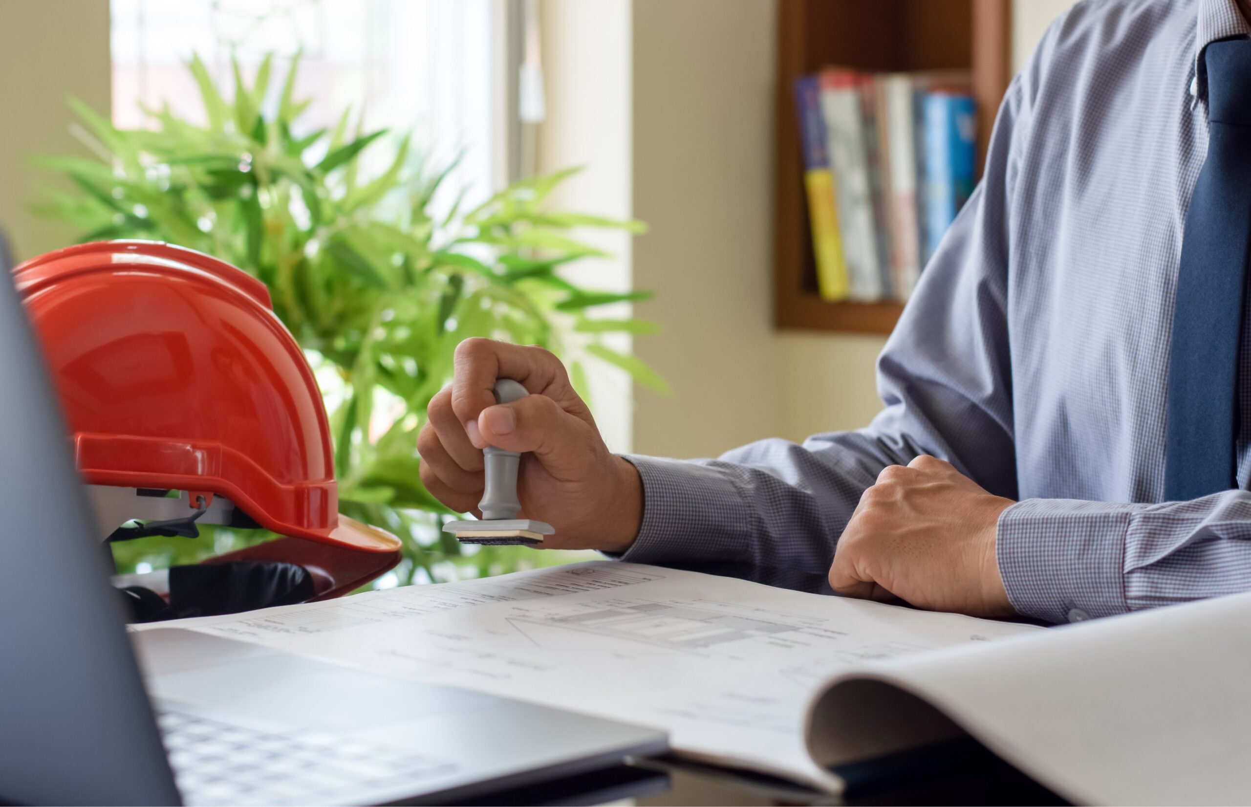 Engineer stamping documents at desk with helmet.